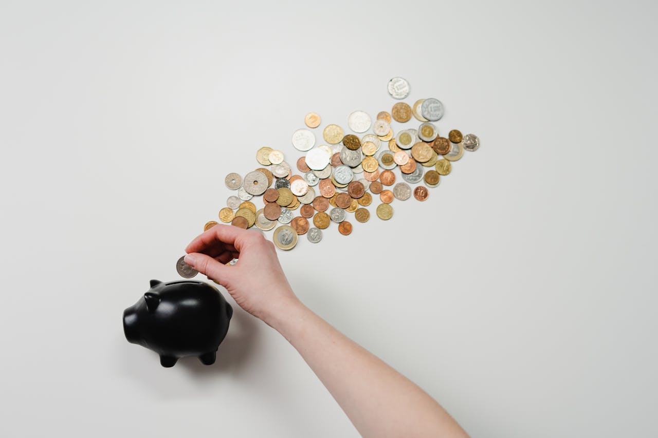 about-02 Person placing coin into a black piggy bank with scattered coins, symbolizing savings and finance.