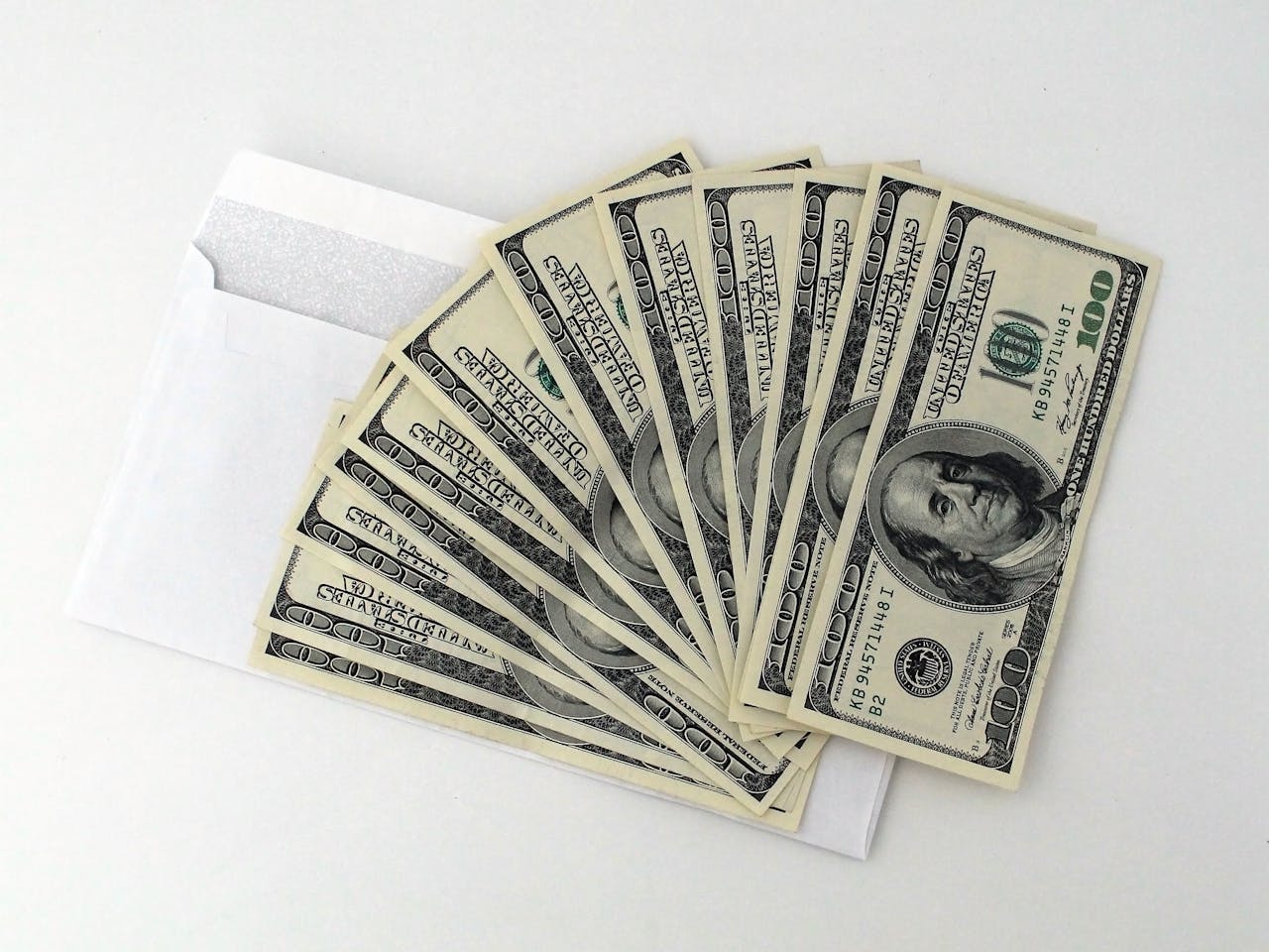 services-img Fan of US $100 bills partially out of a white envelope on a white background.